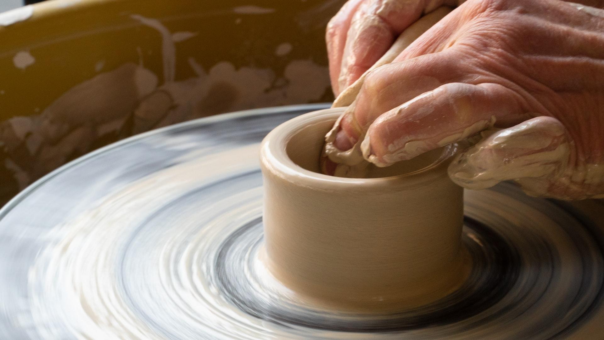 person making clay pot on white round plate