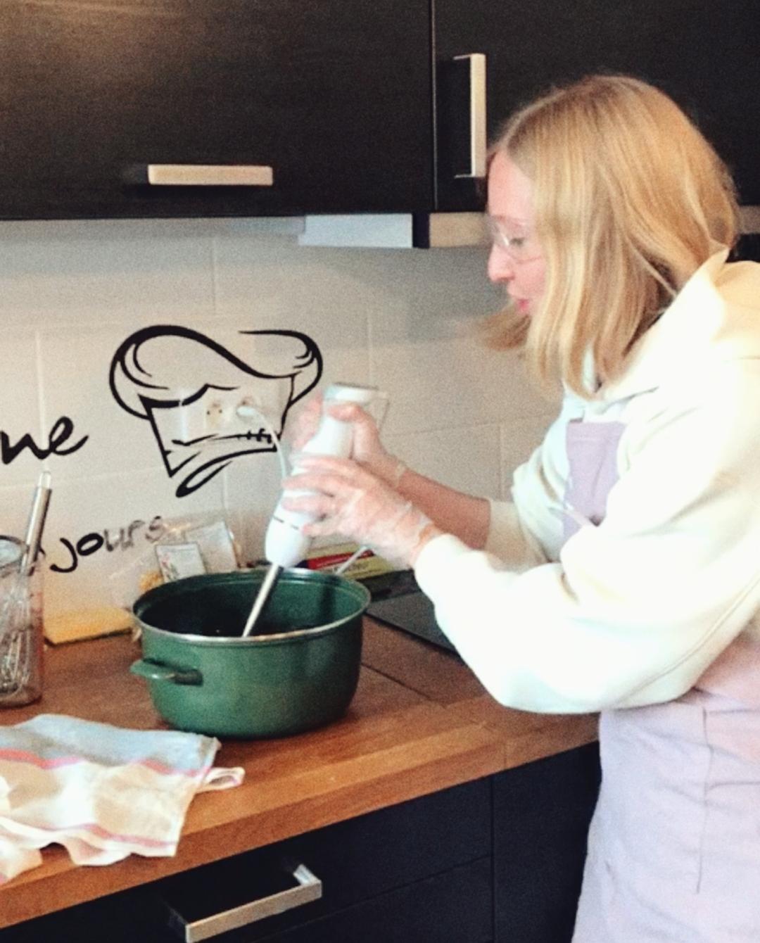 Evgeniya avec un tablier qui mixe une préparation dans une casserole avec un mixer plongent